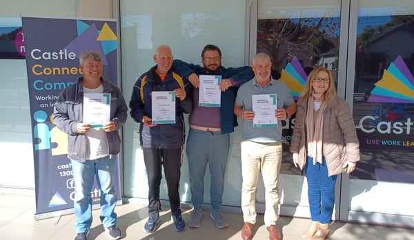 4 men and a woman are standing in front of glass doors, and next to pull-up banner. The 4 men are holding certificates and all are smiling.