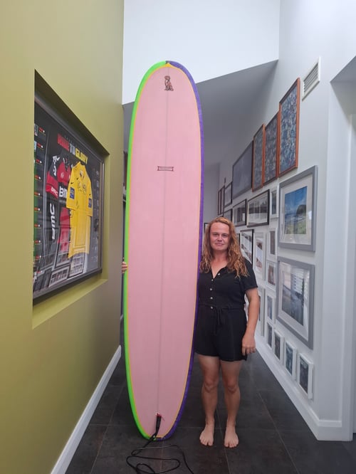 Thea is standing next to a very tall pink longboard.